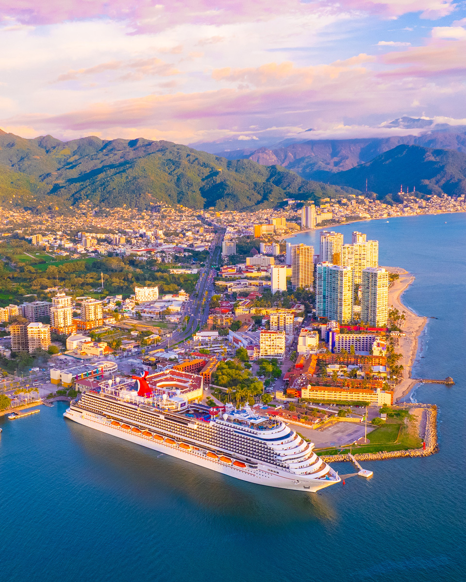 Crucero atracado en el puerto de Puerto Vallarta al atardecer, con la ciudad y la sierra de fondo